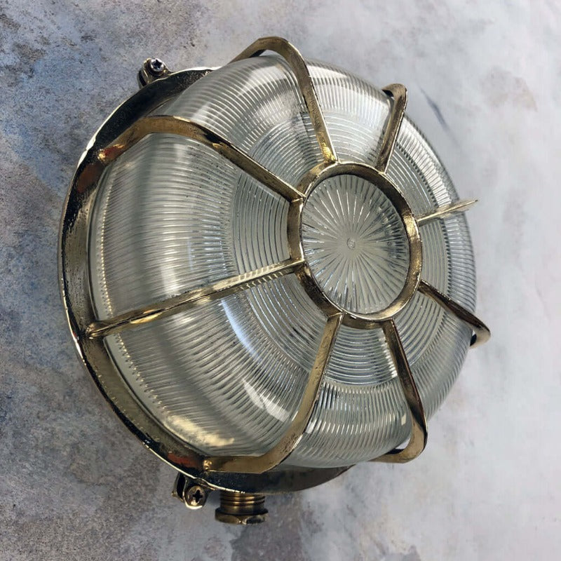 A vintage industrial brass circular bulkhead wall light with target style protective cage over a prismatic glass shade. 